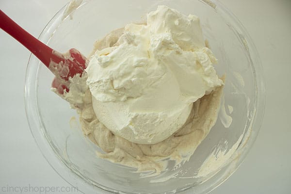 Overhead shot of more ingredients being mixed into the larger clear bowl with a red spatula 