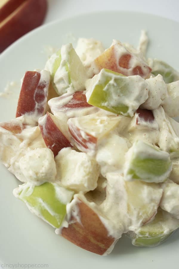 Plated Creamy Apple Salad on a white plate and a white background with the red apple slices showing in the background 