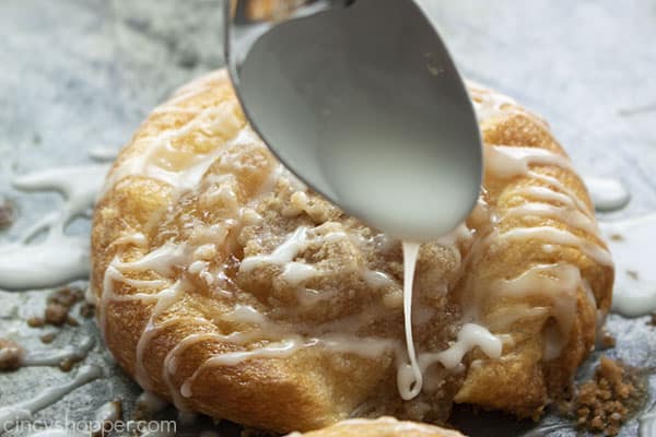 Spoon with icing drizzling on the top of cooked danish