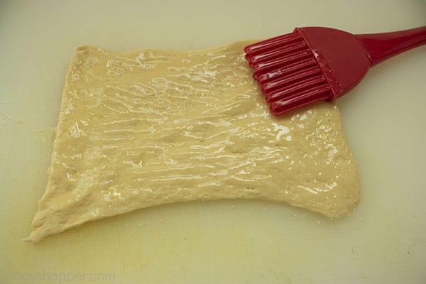 Crescent rolls with butter brushed on top with a red pastry brush.