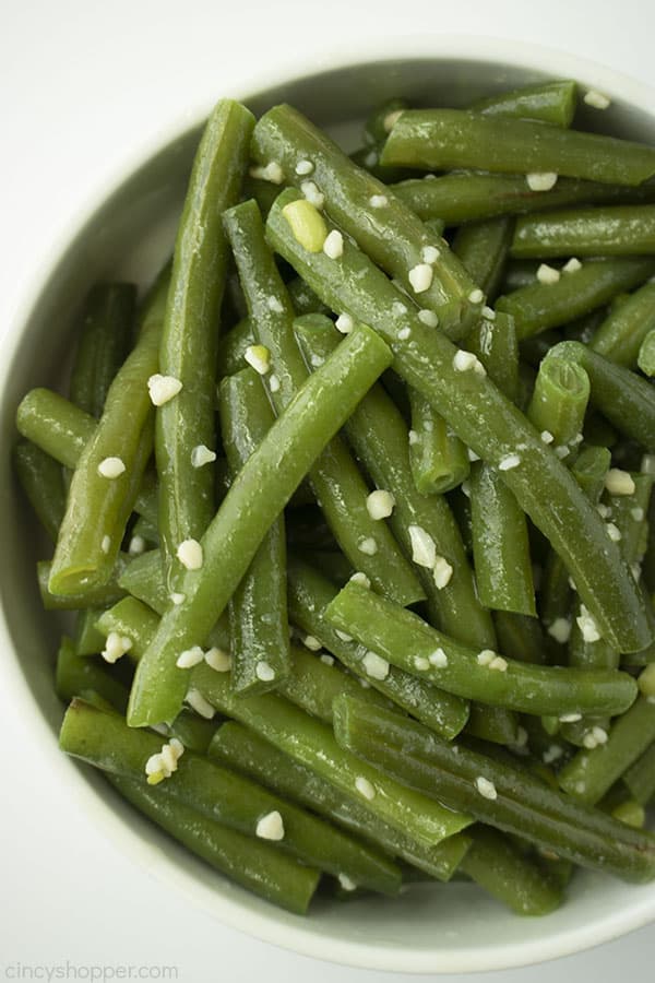 Fresh garlic green beans in a white bowl half of the bowl on white background