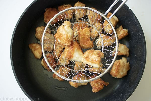 Chicken in a strainer over the top of black skillet.