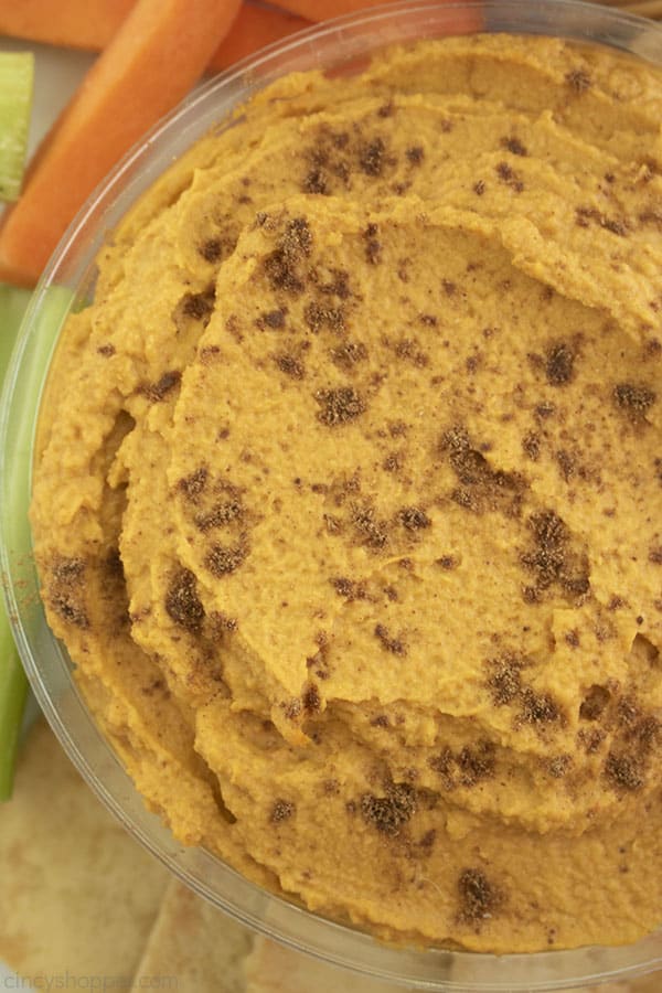 Overhead shot of a clear dish of hummus with carrots, celery, pita chips.