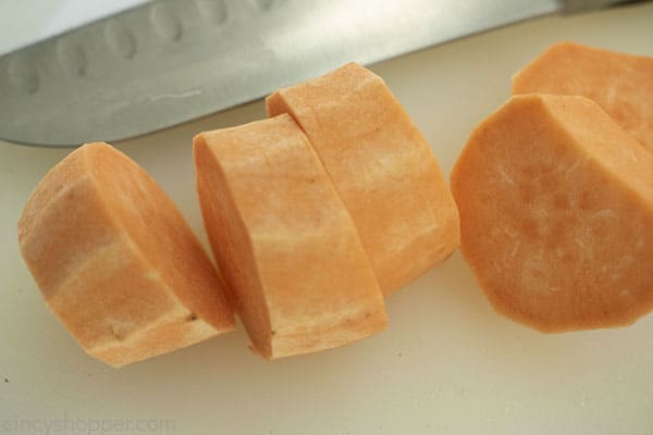 Sliced sweet potatoes on a white cutting board with a knife in background