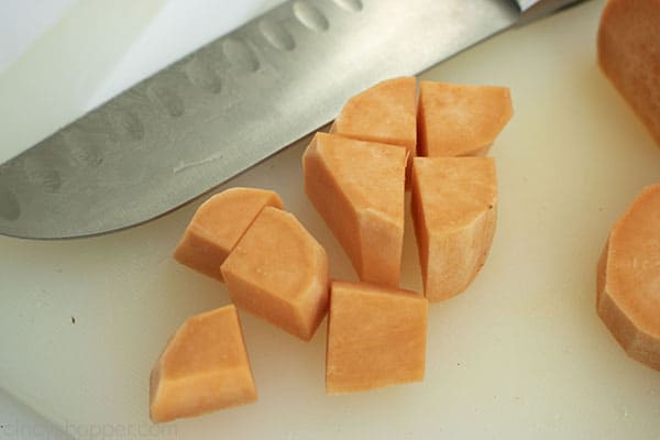 Diced sweet potatoes on a white cutting board with a knife off to the side.