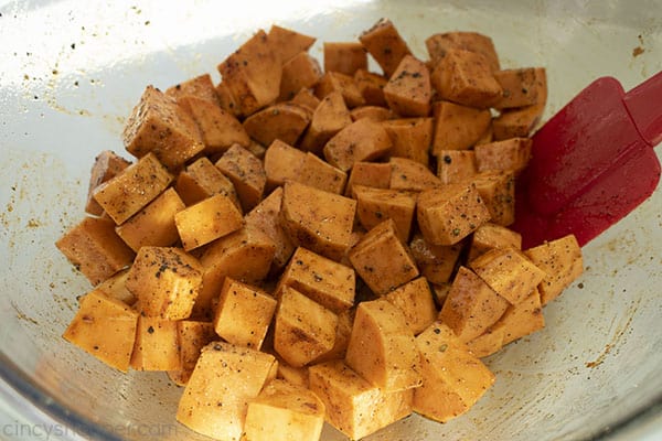 Spice coated sweet potatoes in a clear bowl with a red spatula.