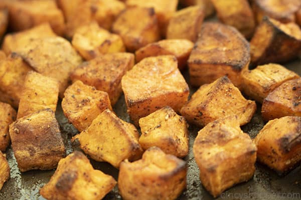 Roasted sweet potatoes on a dark baking sheet.