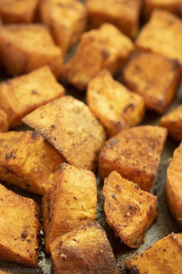 Baked sweet potatoes on a dark sheet pan.