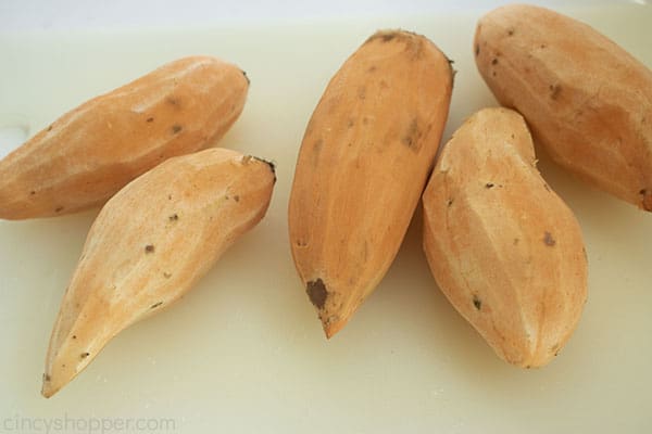 Whole sweet potatoes peeled on a white cutting board.