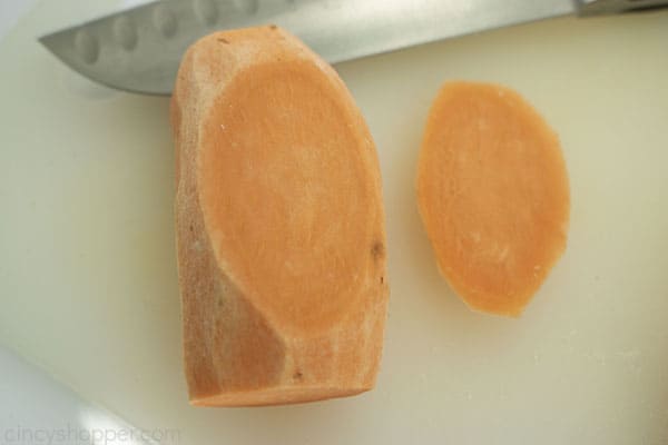 Bottom of sweet potato cut off on a white cutting board with a knife