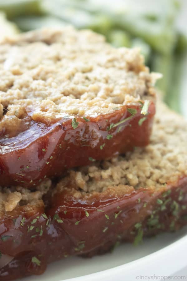 2 pieces of classic meatloaf on a white plate and green beans in the background.