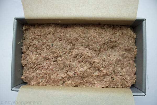 Raw meatloaf in a loaf pan lined with parchment paper.