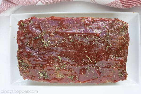 Fully cooked meatloaf on a white platter, white background with red and white towel on edge.