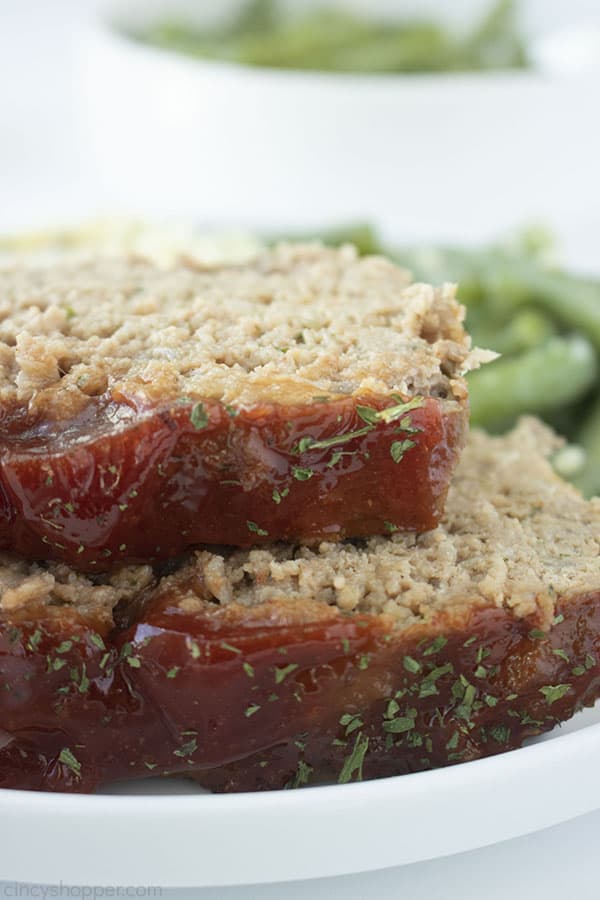 Stack with two pieces of easy meatloaf on a white plate, includes green beans.