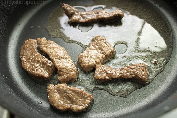 Image of the Mongolian Beef cooking in a large black skillet in vegetable oil