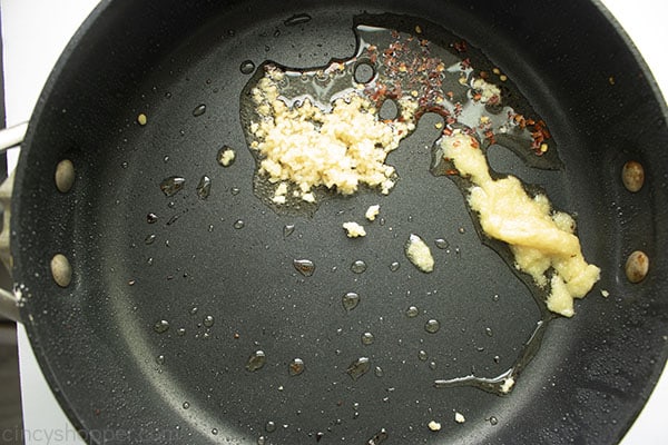 Image of minced garlic, red pepper flakes, and ginger paste cooking in vegetable oil in a large black skillet 