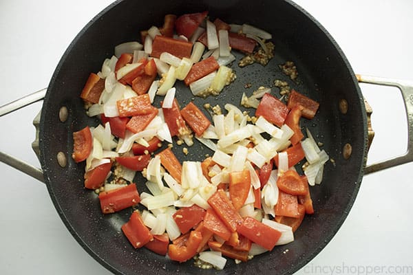 Image of added red peppers and onions cooking in a large black skillet 