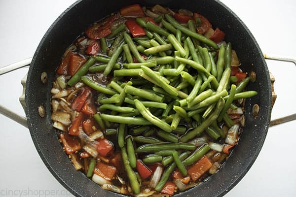Overhead image of green beans being added into the mixture for the Mongolian Beef recipe cooking in a black skillet 