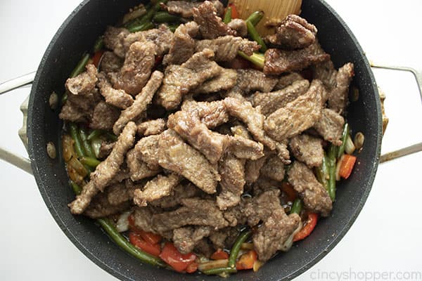 Overhead photo of the cooked Mongolian Beef being added into the large black skillet 