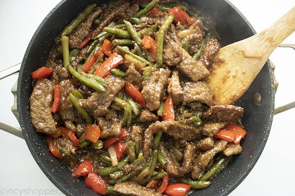 Image of the fully cooked Mongolian Beef recipe in a large black skillet with a wooden spatula on the right hand side 