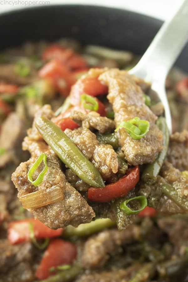 Close up shot showing Mongolian Beef on a white spoon with the dish in the background 