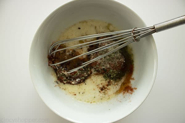 Rotisserie Chicken seasonings and melted butter in a white bowl with a metal whisk