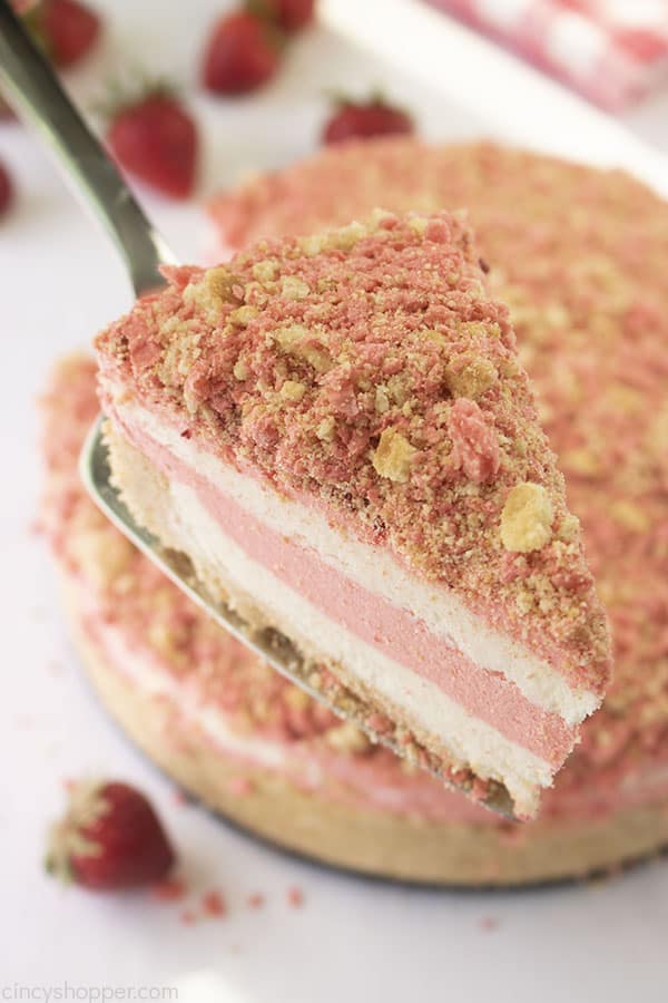up close shot of a pink and white no-bake strawberry crunch cheesecake on a pie server 