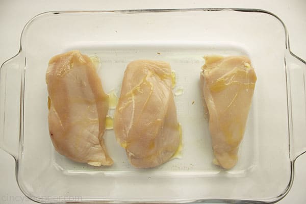 Oil drizzled on raw chicken breats in a clear baking dish