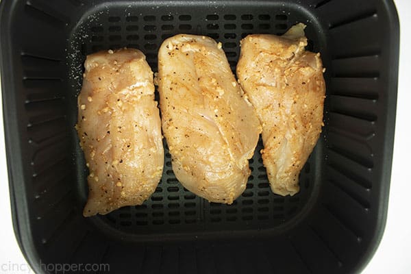 Uncooked and seasoned chicken breasts in a air fryer basket