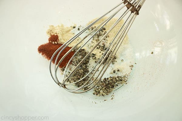 Rub chicken wing spices in clear bowl with wisk
