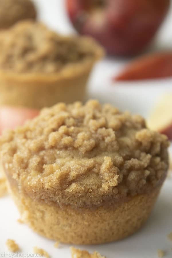 Apple Muffins with crumb topping on a white board with red apple and slices in background