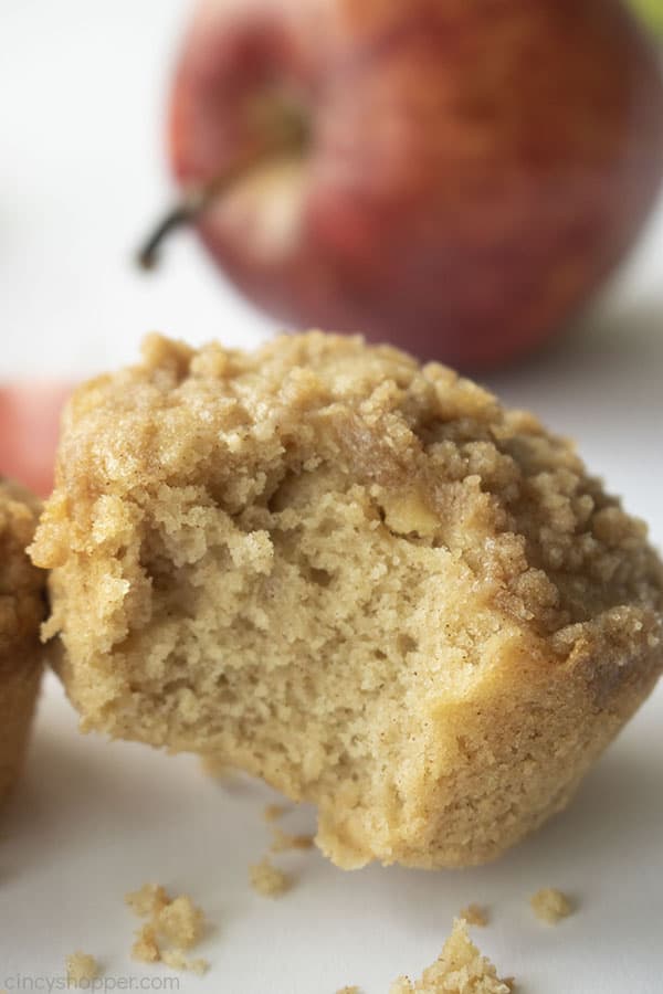 Bite out of crumb muffin on a white background and red apple in the back
