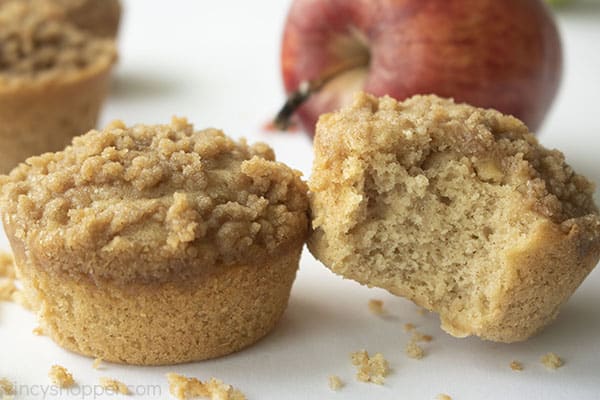 Two muffins with crumbs and apple in the background