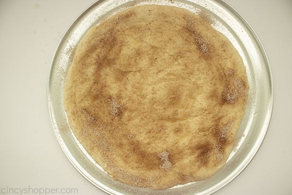 Prepared dessert pizza crust on a round pan with cinnamon sugar topping