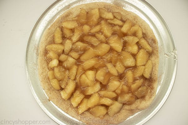 Apple pie filling on a prepared pizza crust on a pan with white bakground