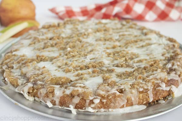 horizontal image of fruit dessert pizza ona pizza pan with white background includes red and white napkin and apple slices