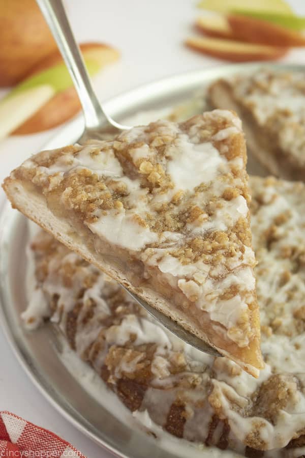 Slice of apple pizza on a pie server with apple slices in background