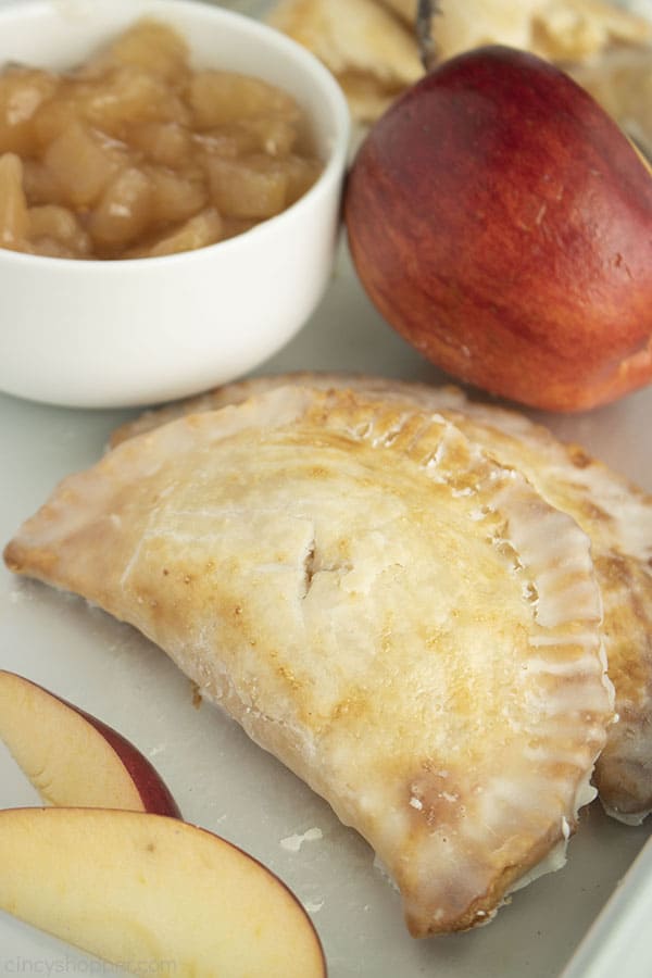 Apple Hand Pies on a pan with apple slices, red apple and bowl of apple pie filling.