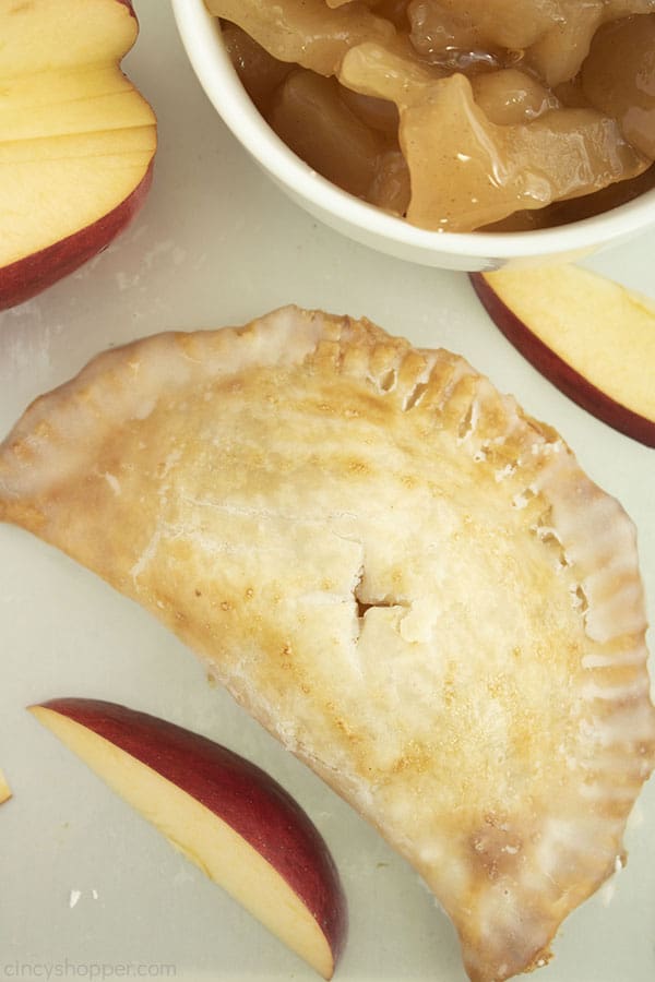 Overhead shot of one apple hand pie with apple slices and apple pie filling in a whit ebowl