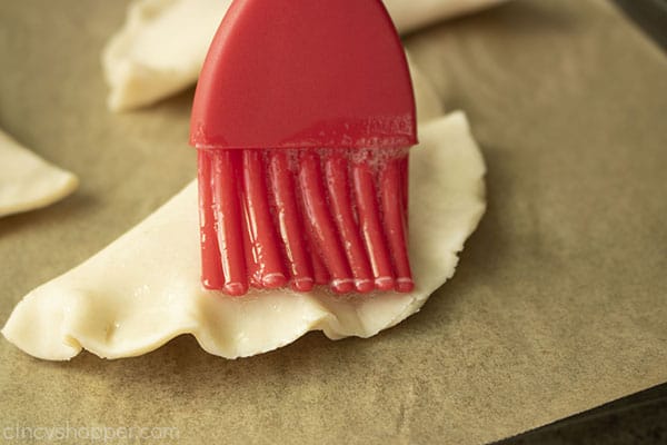 Red pastry brush adding butter to pinched hand pies
