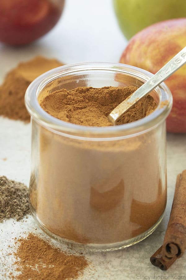 Apple pie spice in a clear jar with a teaspoon apples in the background