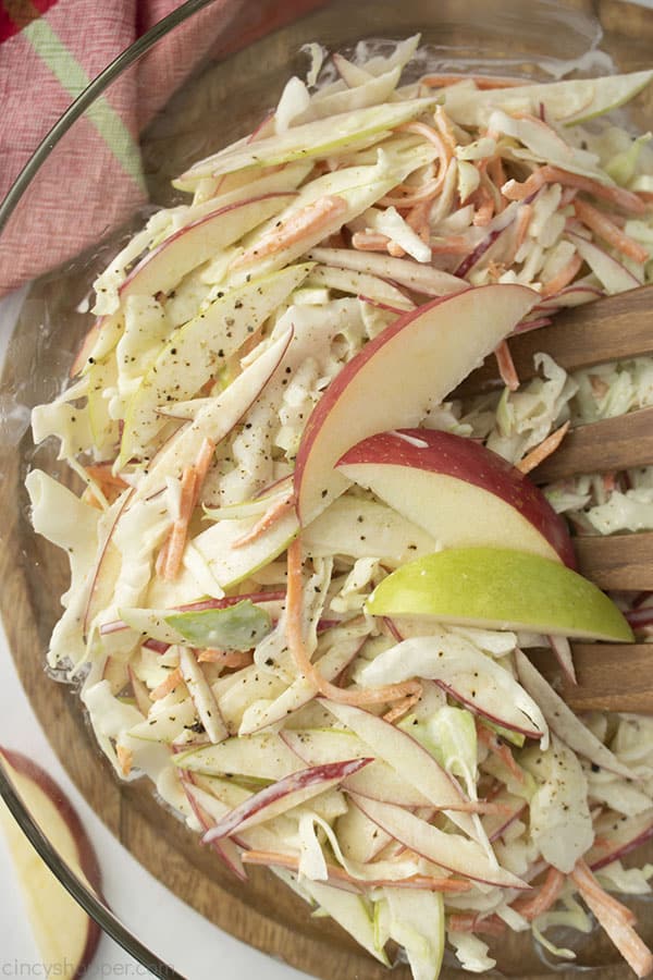 Creamy Apple Slaw in a clear bowl with apple wedges, red napkin and wooden salad fork