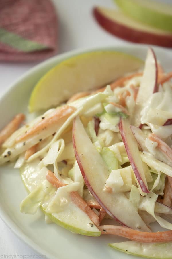 Serving of apple coleslaw on a white plate with napkin and wedges in background