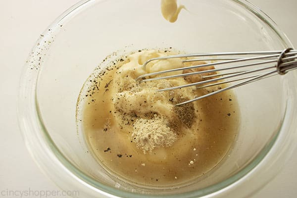 Dressing ingredients in a clear bowl with white background and whisk in bowl