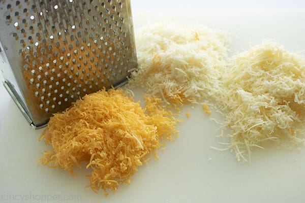 Tree cheeses with grater on a cutting board.