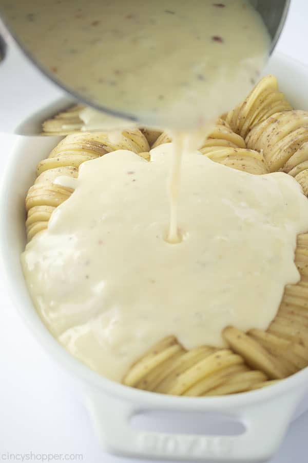 Cheese sauce pouring on sliced potatoes.