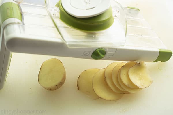 Potatoes being sliced with mandolin slicer.