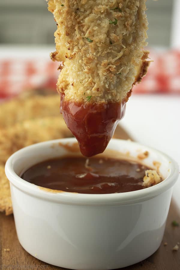 Chicken tender dipped in bbq sauce. White bowl with red and white napkin in the background