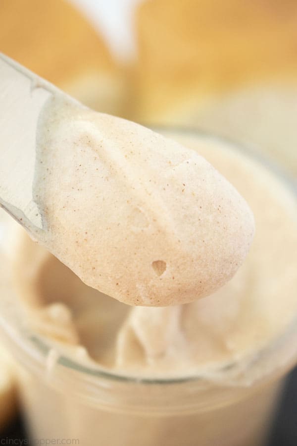 Texas Roadhouse Copycat Cinnamon Butter on a knife with jar and rolls in the background