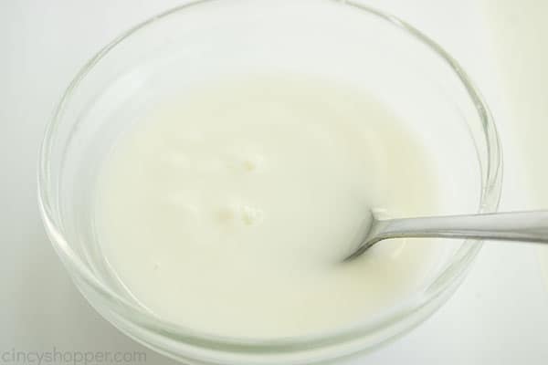Cornstarch slurry in a clear bowl with small spoon, white background.